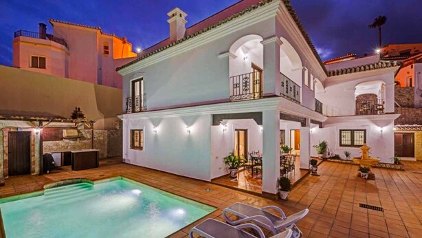 Un edificio de dos pisos con piscina, mobiliario exterior y un patio bien iluminado.