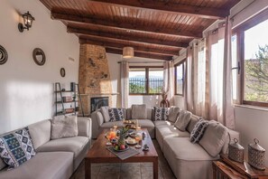 Una sala de estar acogedora con chimenea de piedra, techo de madera y un amplio ventanal con vistas a la montaña.