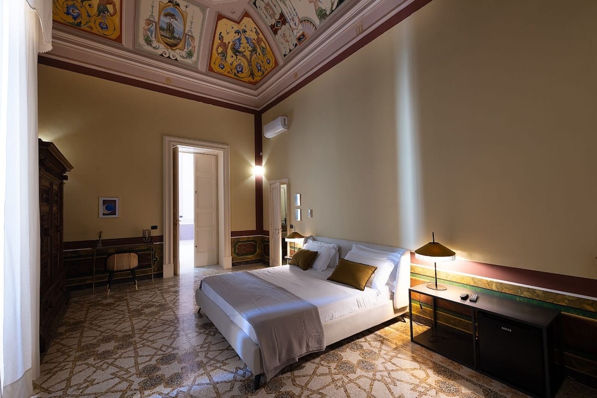 Een hotelkamer met een groot bed, een bureau, een stoel en een decoratief plafond.