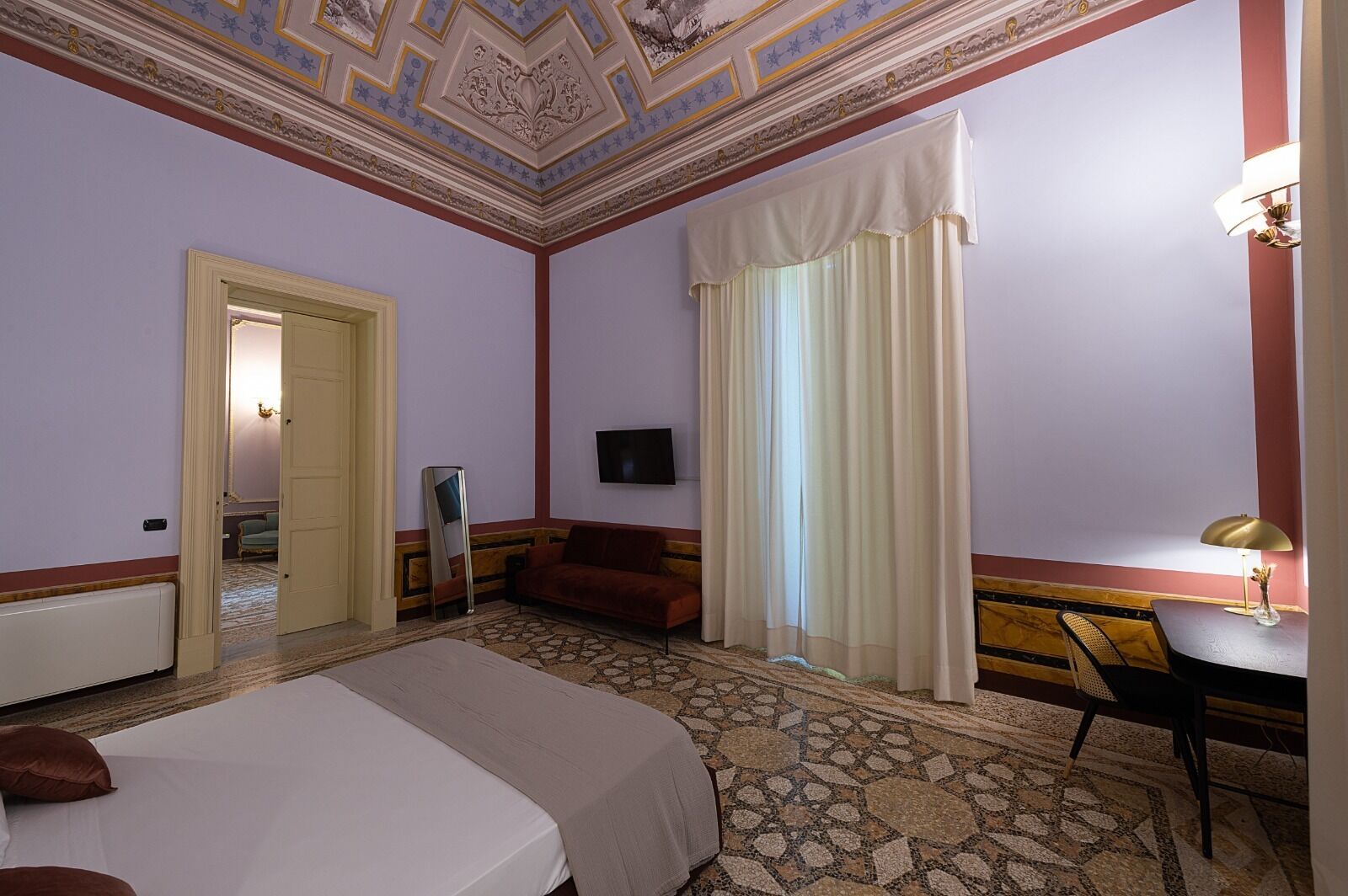 A hotel room with a bed, a desk, a chair, a TV, and a mirror.