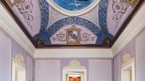 Een ruime kamer met een groot, versierd plafond, een patroon vloer en een centrale deuropening.