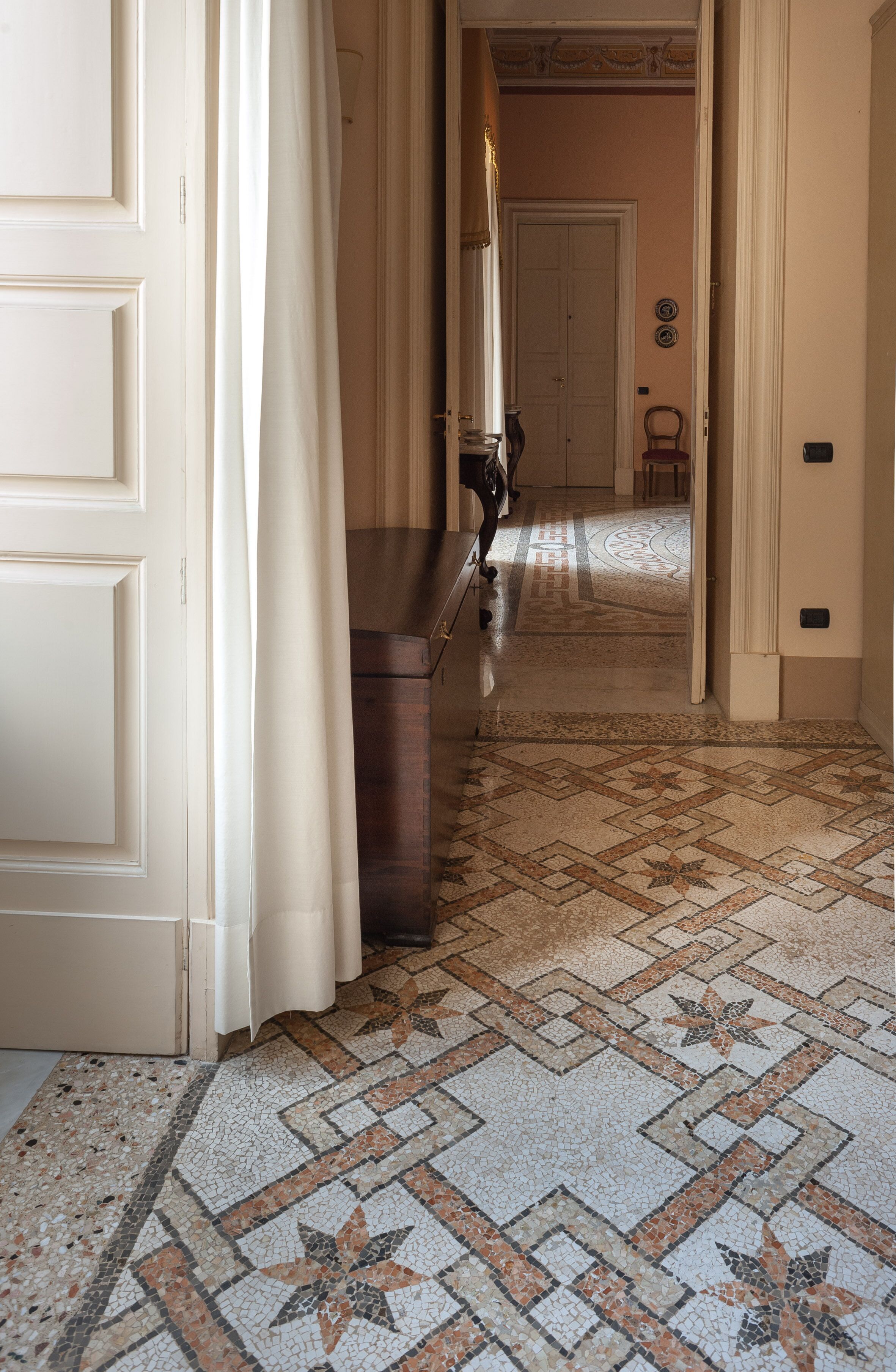 A hallway with a patterned floor, a wooden bench, and a door with a curtain.