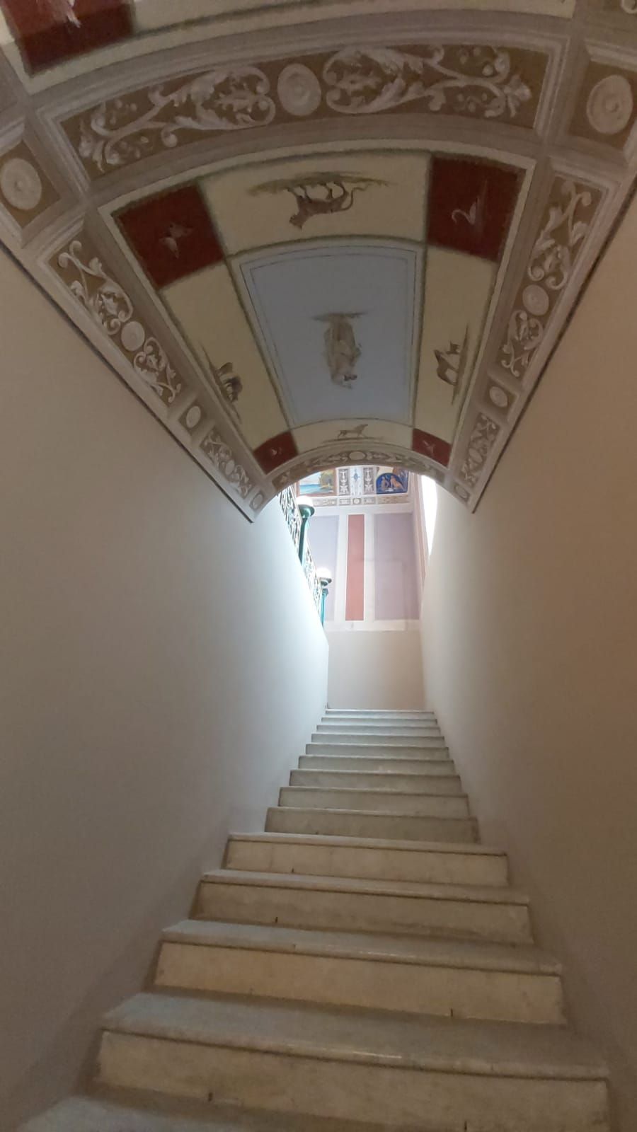 A staircase with a decorative ceiling and a view of a room at the top.