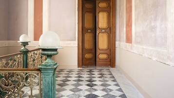 A hallway with a checkered floor, ornate metal railings, and a wooden door.