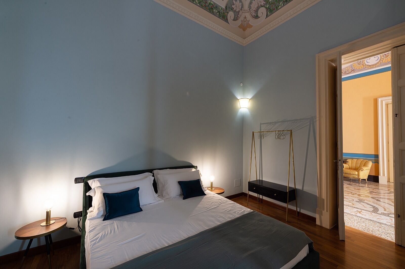 A bedroom with a bed, bedside tables, a wall-mounted light, and a door leading to another room.