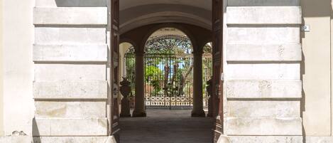 Una entrada arqueada con una reja de hierro forjado, que conduce a un patio con una fuente y follaje.