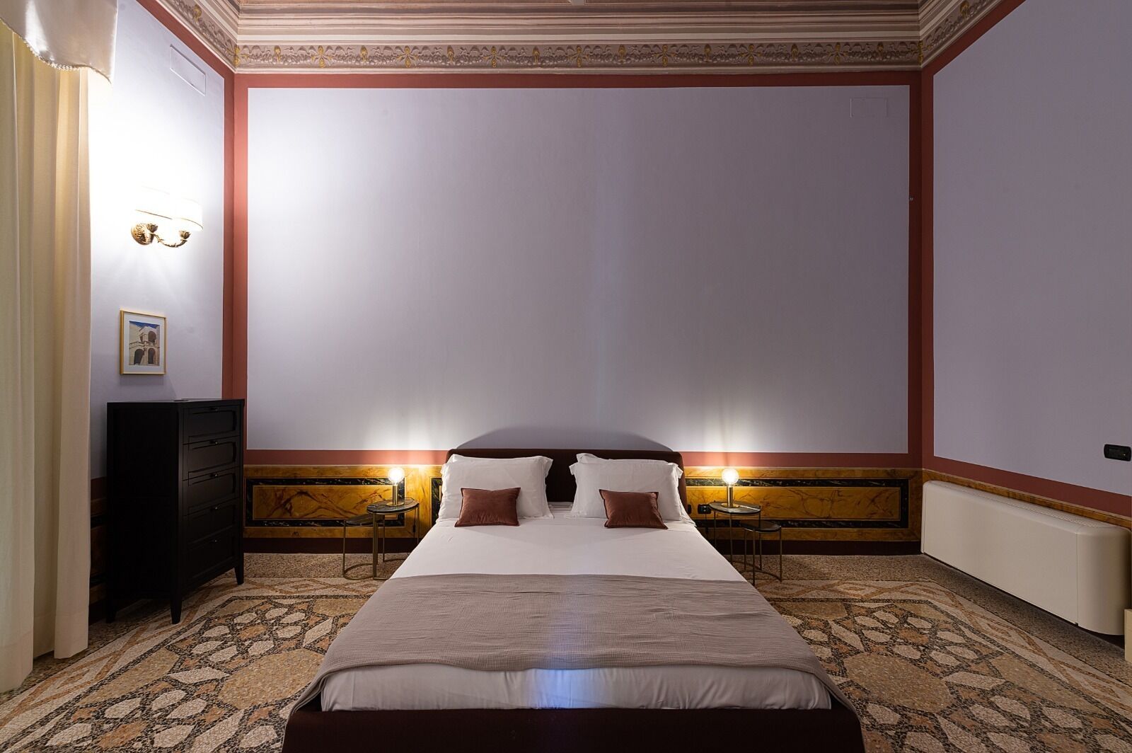 Una habitación de hotel con una cama grande, dos lámparas de noche, un aparador y suelo alfombrado.