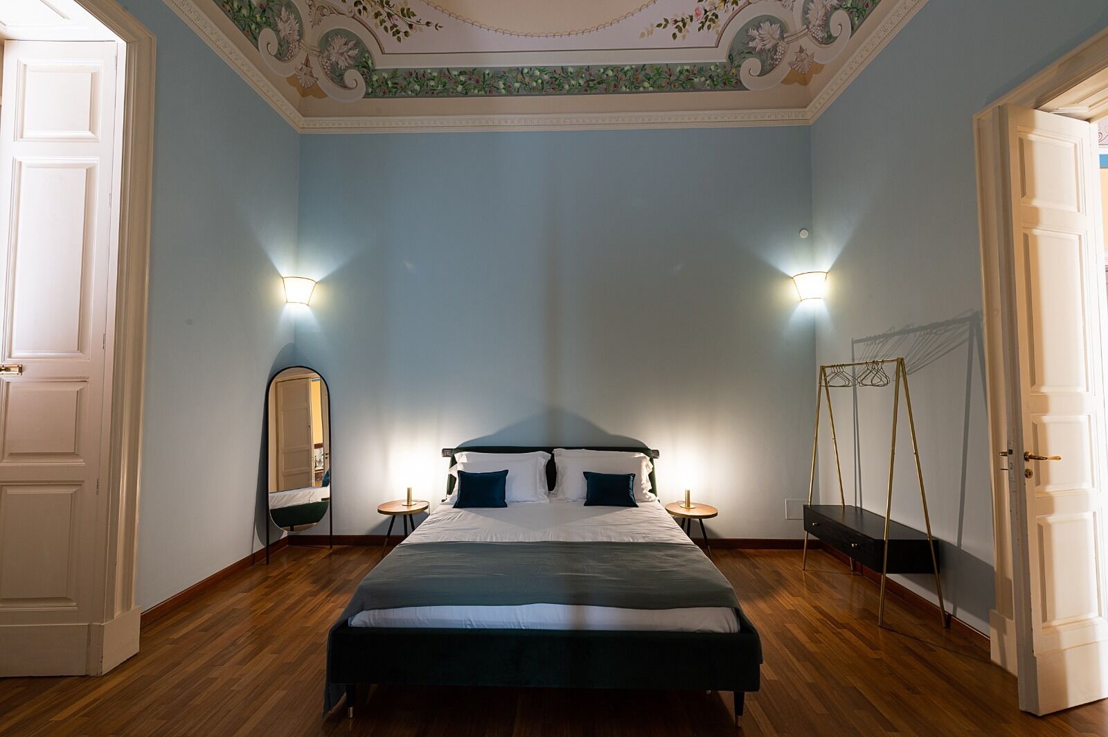 A bedroom with a bed, two bedside tables, a mirror, a hanging light fixture, and a wardrobe.