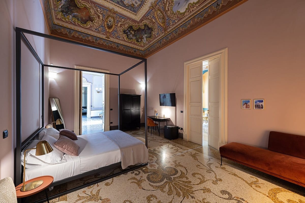 Een slaapkamer met een hemelbed, een bureau met stoel, een televisie en een bank.