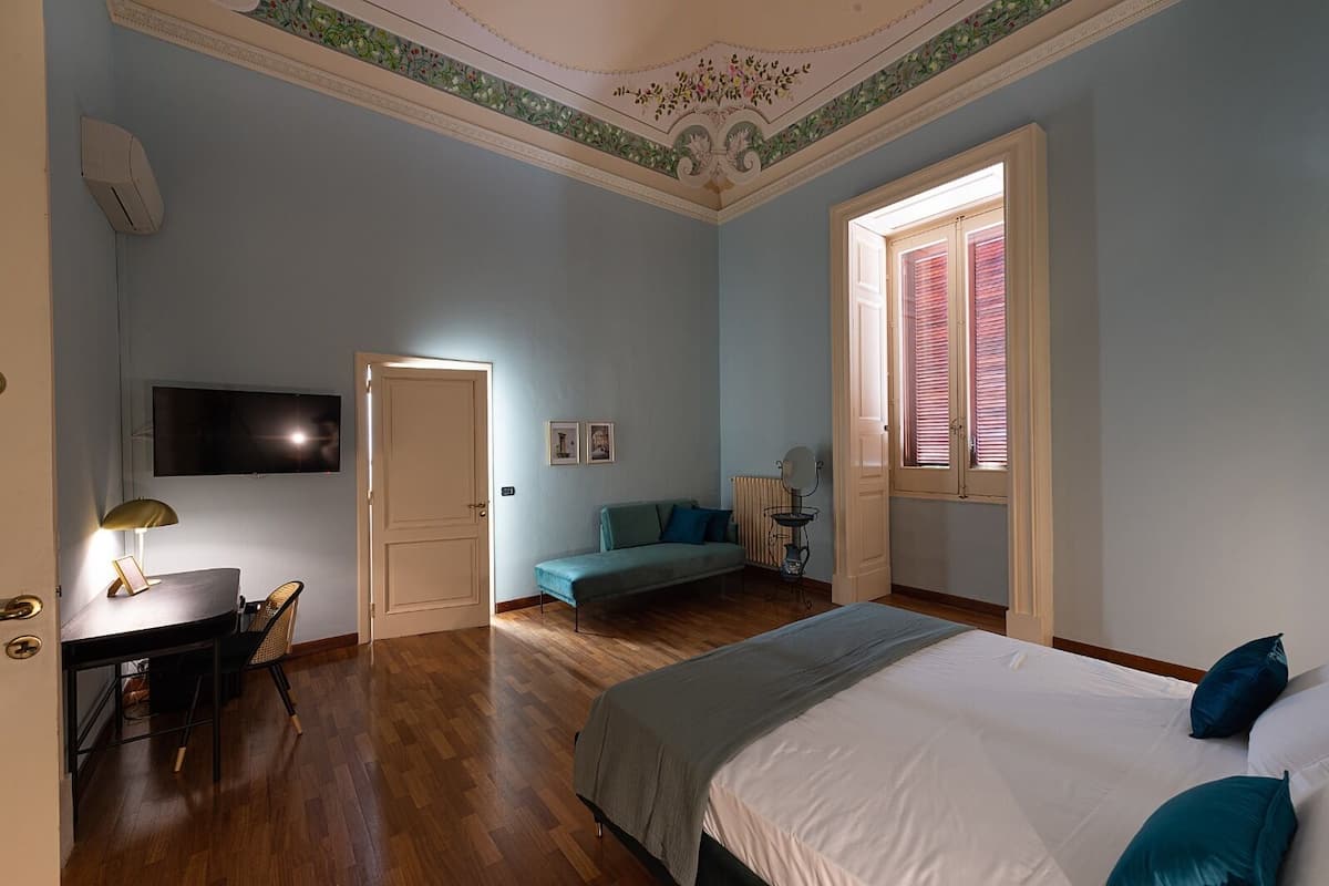 Een slaapkamer met een bed, een bureau met stoel, een televisie en een raam met luiken.