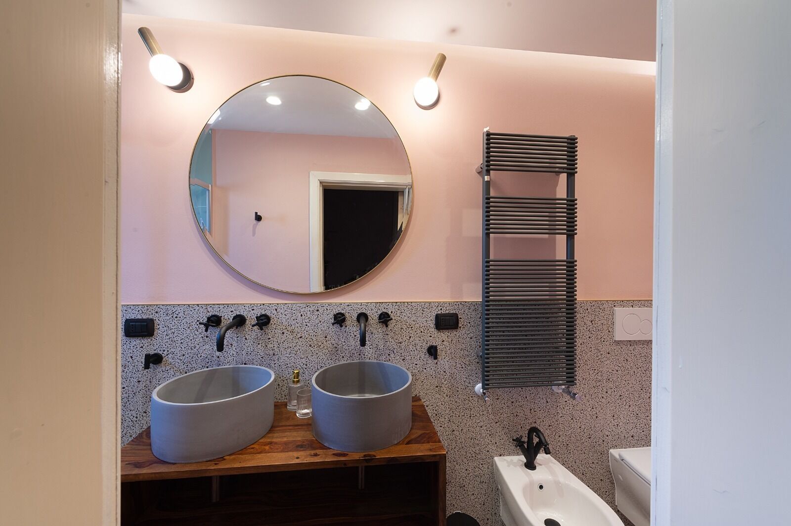 A bathroom with two sinks, a round mirror, and a towel rack.