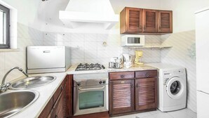 A compact kitchen with a gas stove, oven, microwave, and a washing machine. - Casa Nomanico - Two Bedroom Villa, Sleeps 4 (Estoi)