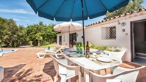 An outdoor patio with a table set for dining, surrounded by white chairs, under a blue umbrella. - Casa Nomanico - Two Bedroom Villa, Sleeps 4 (Estoi)