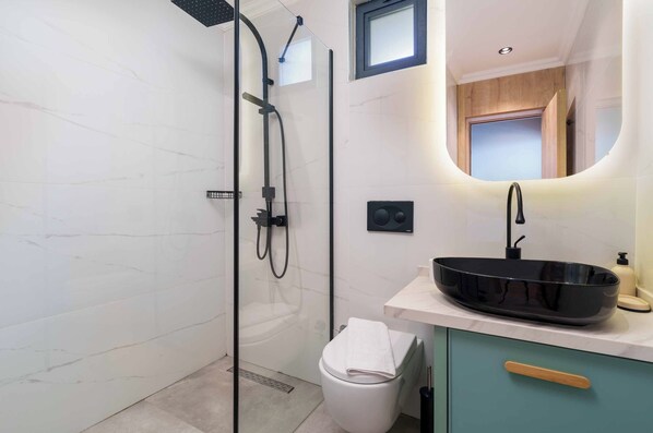 A modern bathroom with a glass-enclosed shower, a black vessel sink, and a wooden cabinet.