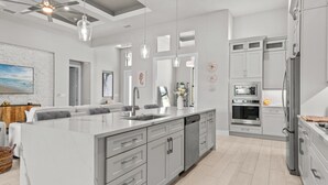 Une cuisine moderne dotée d’un grand îlot central, d’appareils électroménagers en acier inoxydable et de luminaires suspendus.