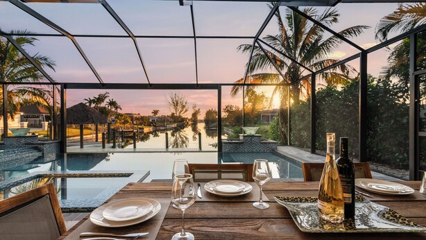 Une table à manger dressée pour deux personnes, avec vue sur une piscine et des palmiers.
