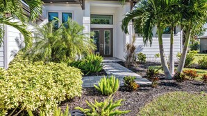 Une maison moderne dotée d’un jardin bien entretenu, comprenant divers arbustes et palmiers.