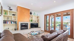 A living room with a fireplace, television, bookshelves, and a leather sofa. - Ca l Berros - Three Bedroom Villa, Sleeps 6 (Alcúdia)