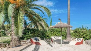 A beach with palm trees, a thatched-roof hut, and two signs with symbols. - Ca l Berros - Three Bedroom Villa, Sleeps 6 (Alcúdia)