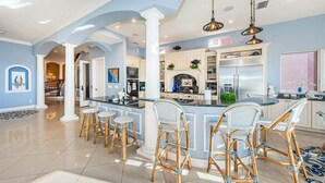A spacious kitchen with a central island, white cabinetry, and a dining area with wicker chairs.