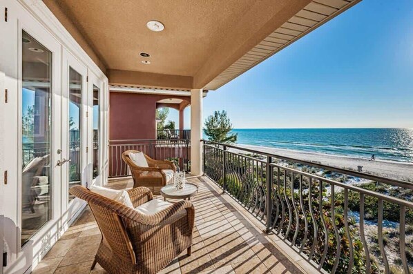 A balcony with wicker furniture, a view of the ocean, and a clear sky.