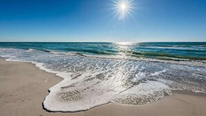 A beach with waves, a clear sky, and the sun shining.