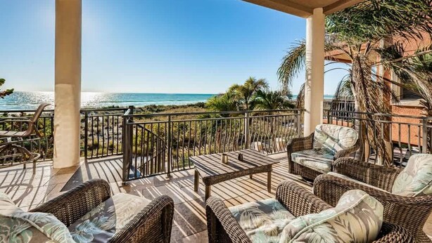 A covered outdoor area with wicker furniture, a table, and a view of the beach.