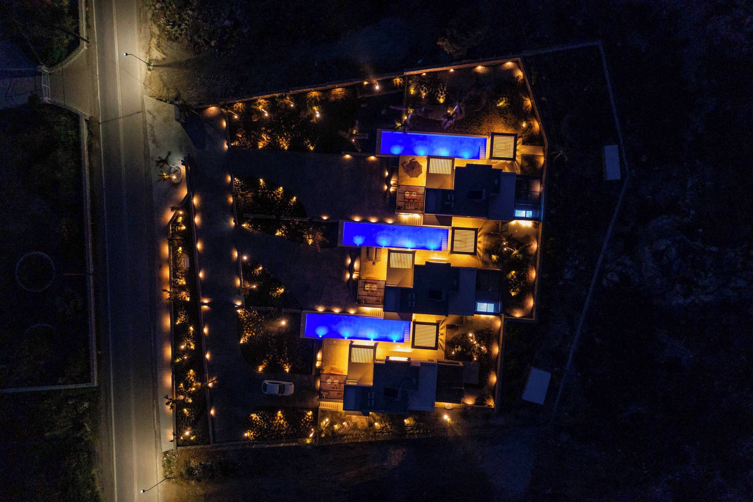 Vista aérea de um hotel com vários quartos, piscina e iluminação externa.