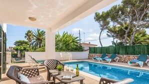 A covered outdoor area with a pool, lounge chairs, and a table with a bottle and glasses. - Villa Cati Punta Prima (Punta Prima)