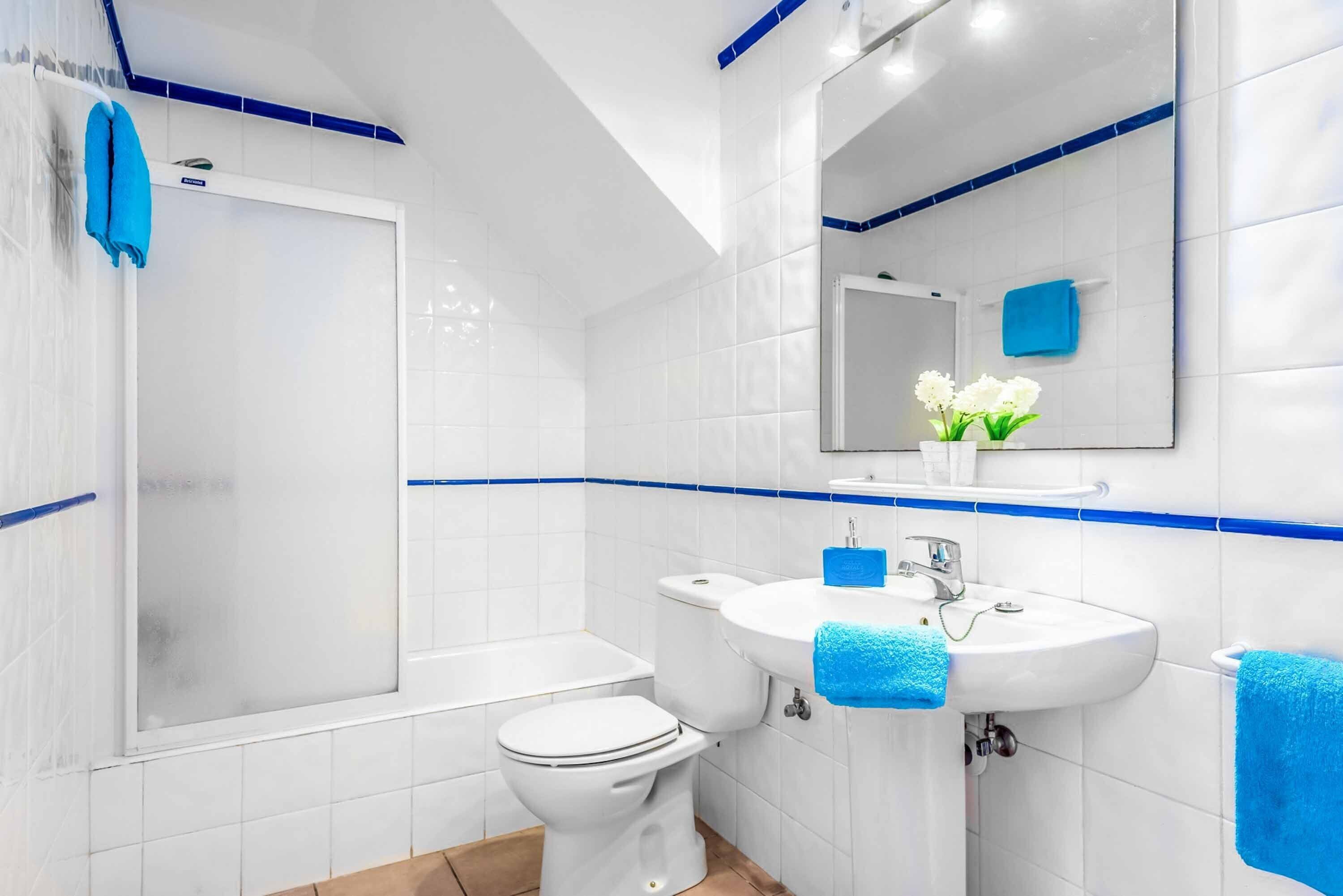 Een badkamer met witte tegels, een bad, een toilet, een wastafel en een spiegel.