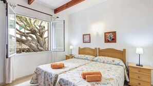 A bedroom with two beds, a window with a view of a tree, and two bedside tables with lamps. - Villa Bini Beatriz - Two Bedroom Villa, Sleeps 4 (Binibeca)