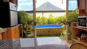 Une cuisine équipée d’un réfrigérateur, un coin repas avec des chaises, une piscine bordée d’un mur en pierre et une vue sur une montagne.