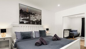 Een moderne slaapkamer met een groot bed, een nachtkastje met een lamp, een bijzettafeltje en uitzicht op de Eiffeltoren.