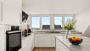Een moderne keuken met witte kasten, een zwarte oven, een spoelbak en een raam met uitzicht op een huis.