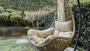 Una silla colgante en un jardín con un estanque y abundante vegetación.