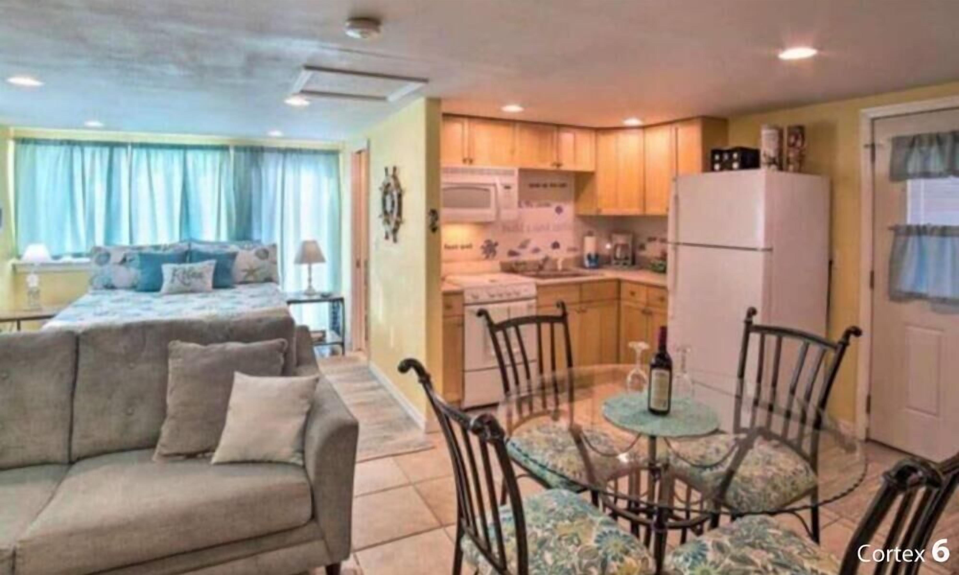 Un espacio habitable compacto con sofá, una mesa de comedor con sillas, kitchenette y cama.