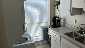 Eine kompakte Küche mit eingebauter Waschmaschine, Spüle und Fenster mit Jalousien.