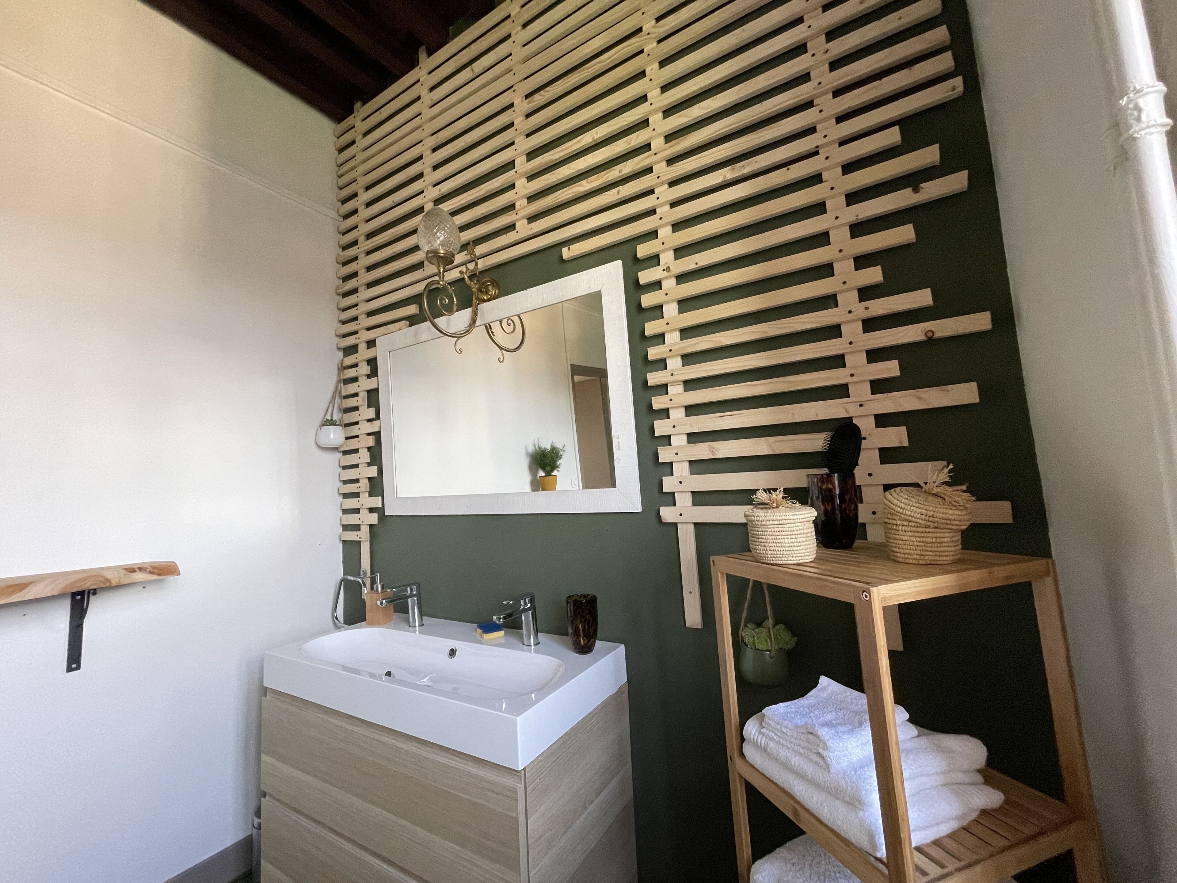 Een badkamer met een wand van houten latten, een wit wastafelmeubel en een spiegel.