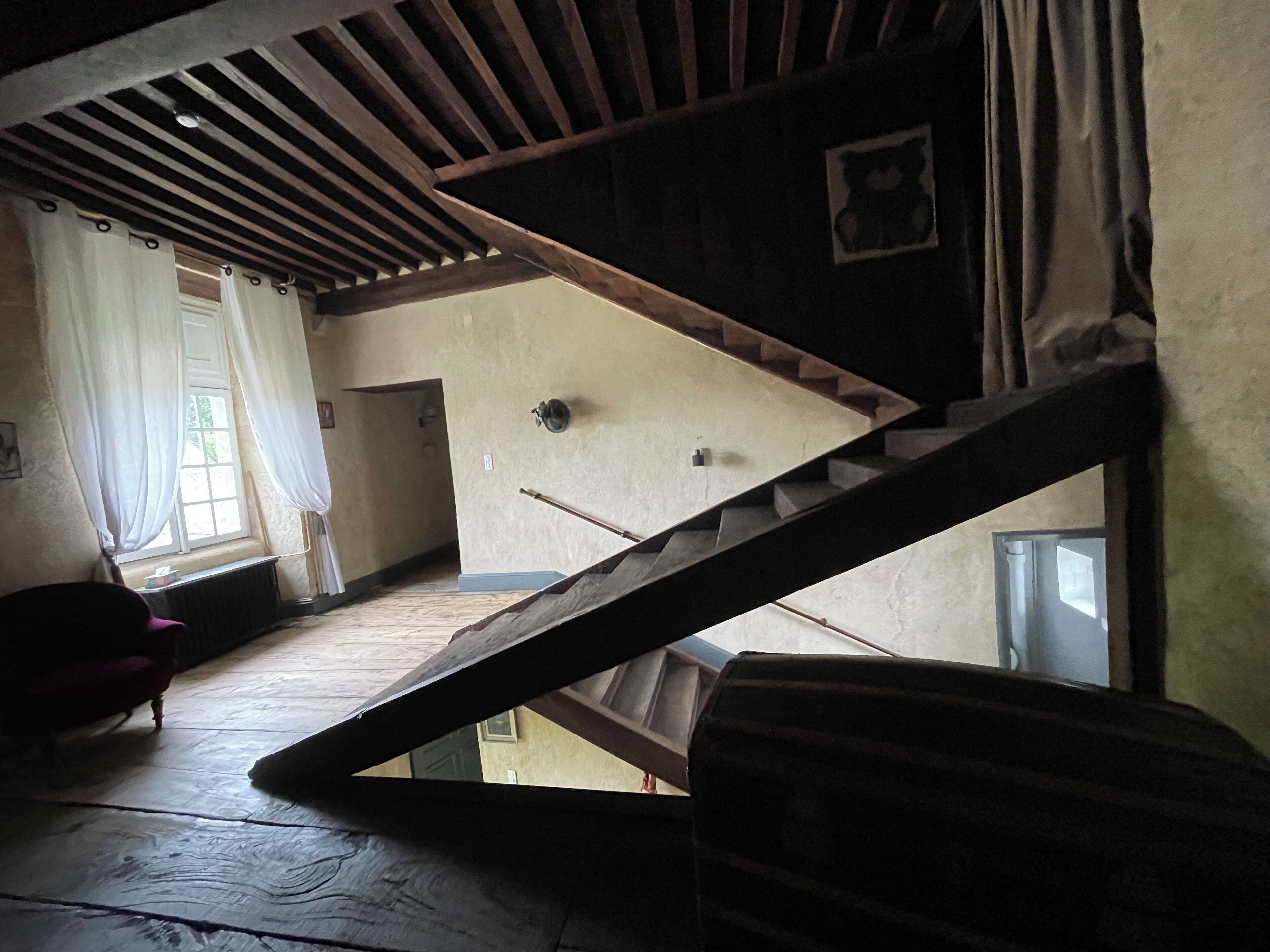 A room with a sloped ceiling, a staircase, and a window with curtains.