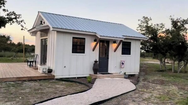 A small white building with a metal roof, a porch, and a pathway leading to the entrance.