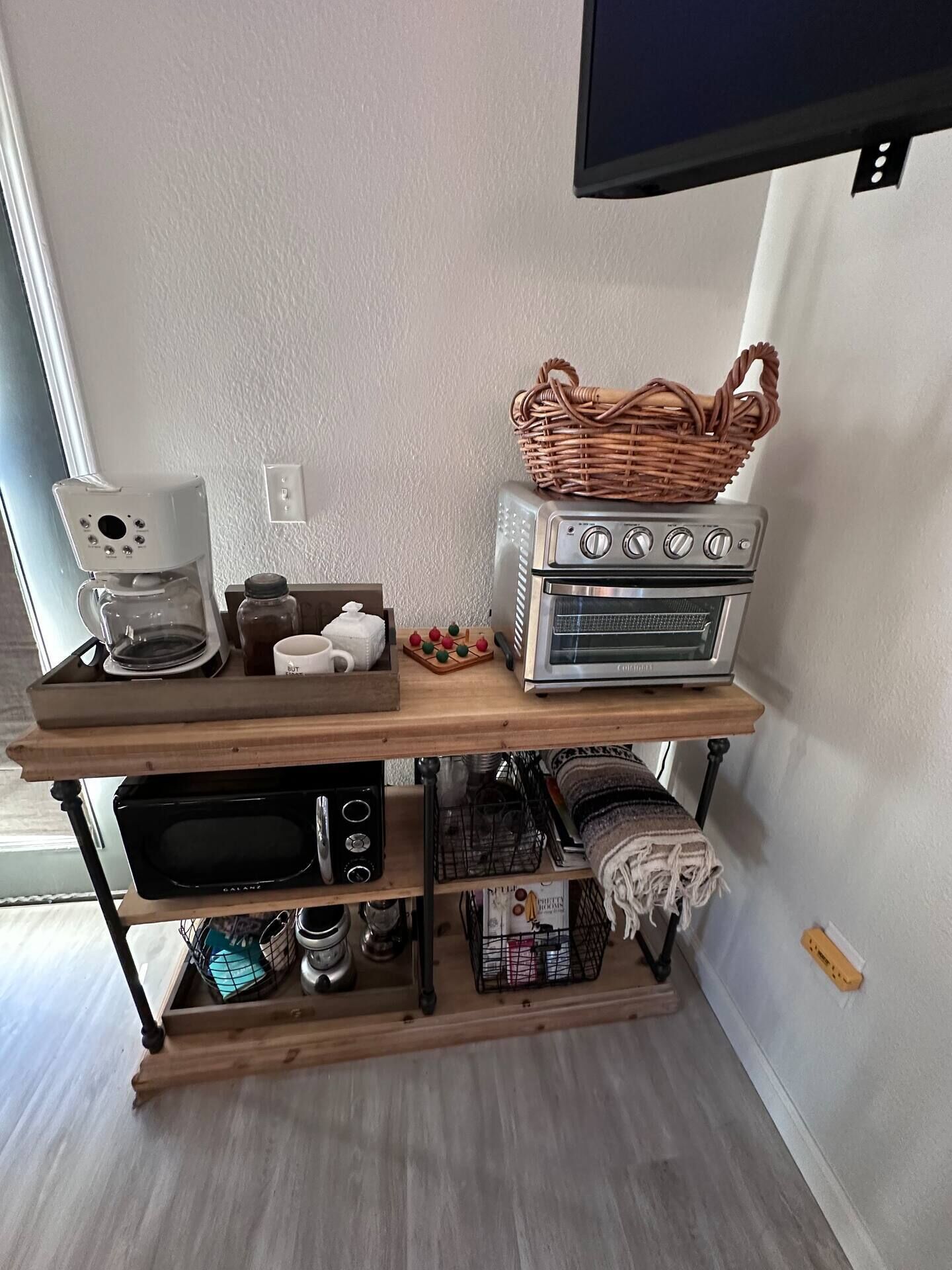 Una cocina equipada con cafetera, tostadora, microondas y horno sobre un estante de madera.