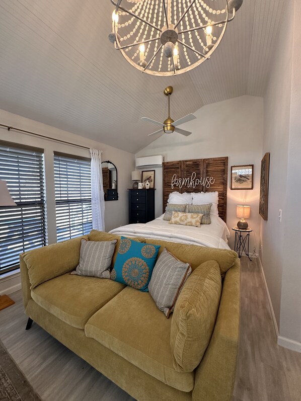 A bedroom with a bed, a ceiling fan, a chandelier, a sofa, and a wall-mounted side table. - Cottage at Hilltop Estates

 (Fredericksburg)
