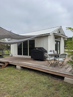 A covered outdoor patio with a grill, dining table, and chairs. - Cottage at Hilltop Estates

 (Fredericksburg)