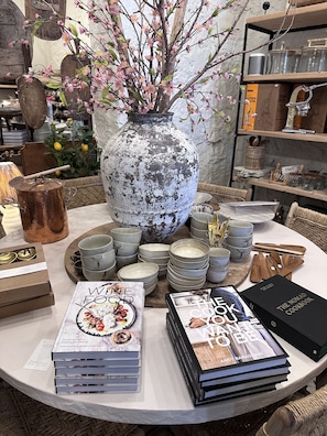 Uma mesa com tigelas de cerâmica, um vaso com flores cor-de-rosa e livros intitulados 'The Nomad Cookbook' e 'Wine & Food'.