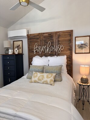 A bedroom with a bed, a dresser, a lamp, and a wall-mounted sign that reads "farmhouse". - Cottage at Hilltop Estates

 (Fredericksburg)