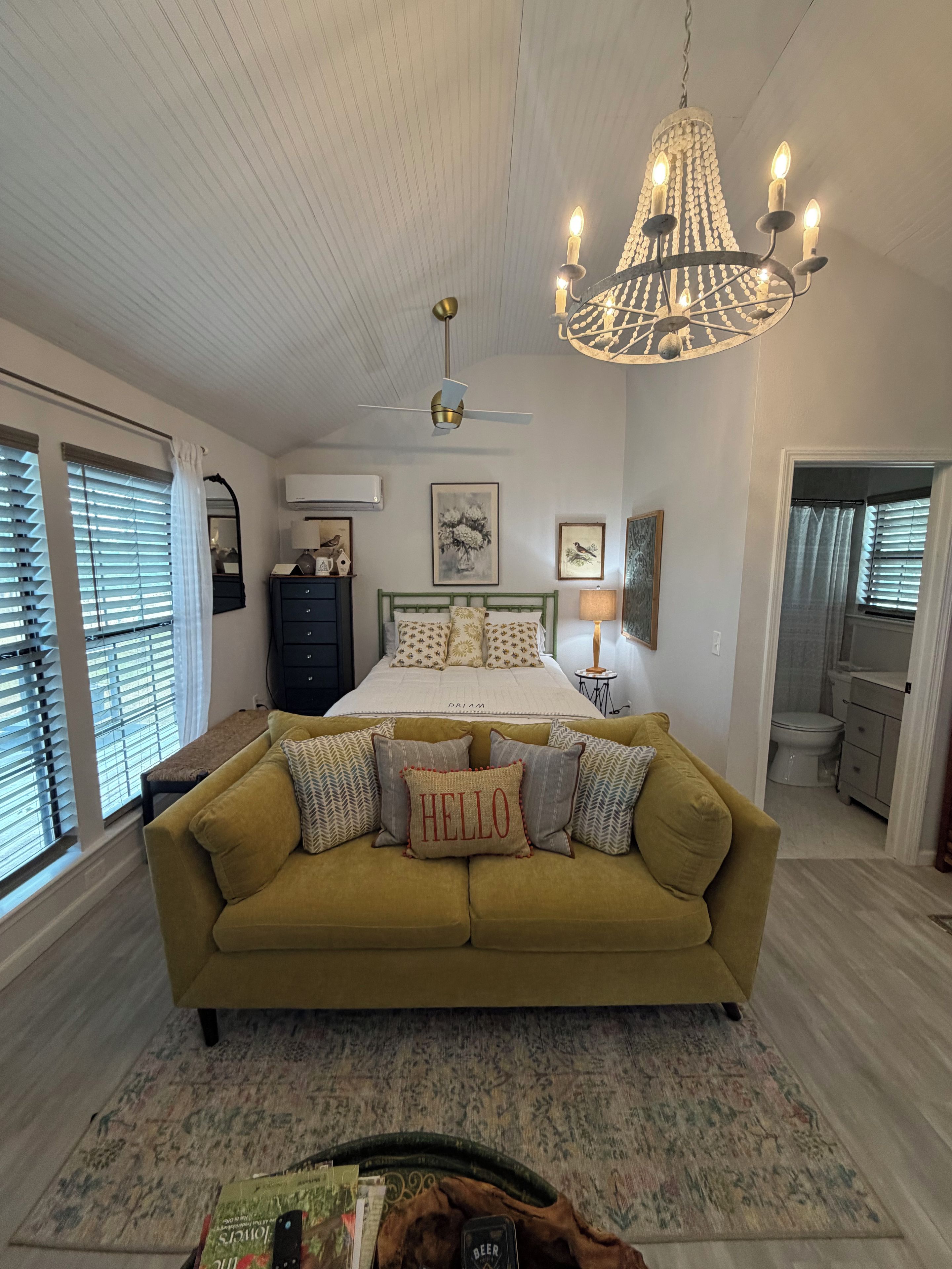 A bedroom with a bed, a green sofa, a chandelier, and a ceiling fan.