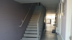 Una scala conduce a un livello superiore in un edificio, con ringhiera metallica e tappetino blu alla base.