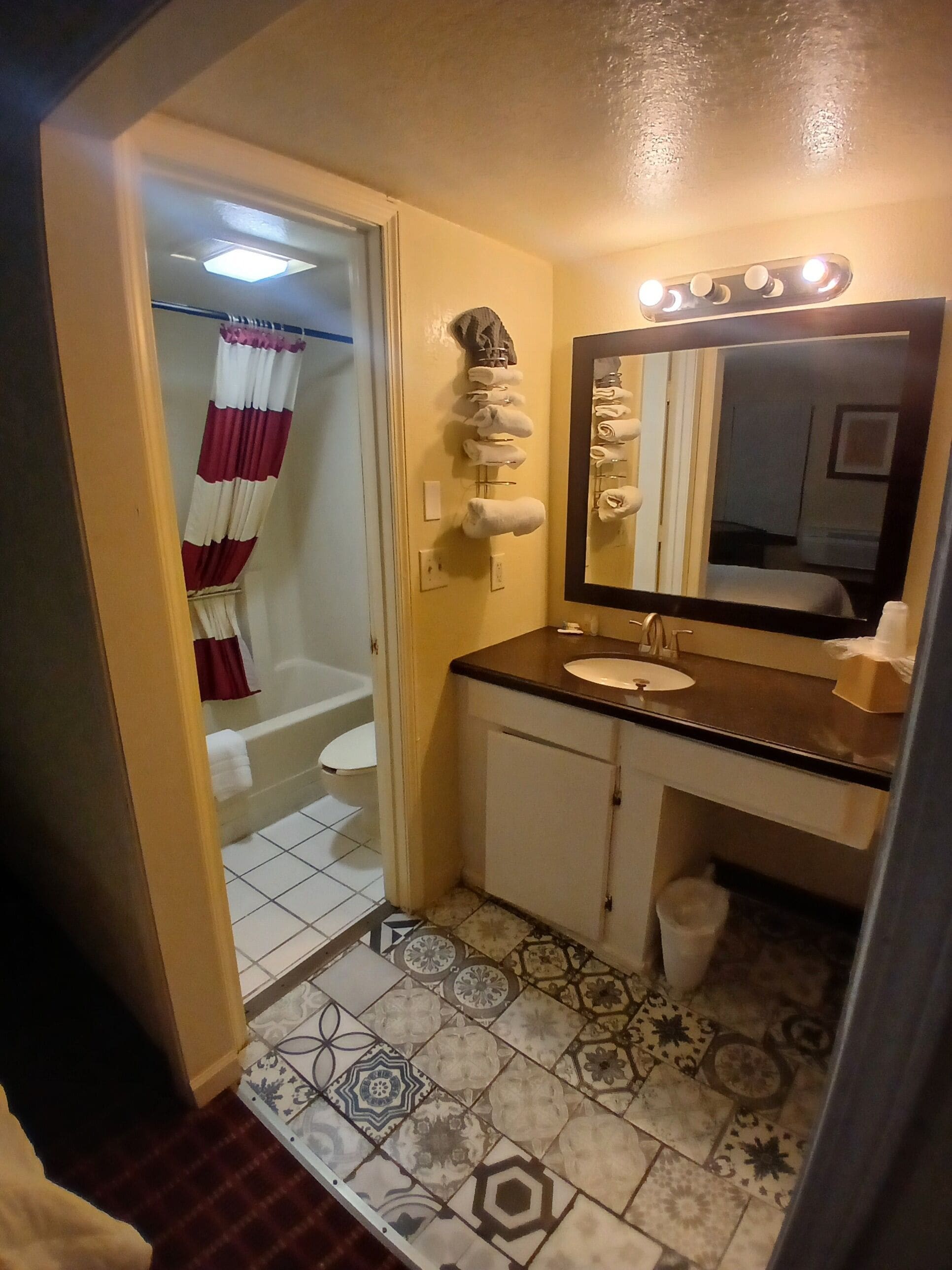 A bathroom with a bathtub, a sink, a mirror, and patterned floor tiles.