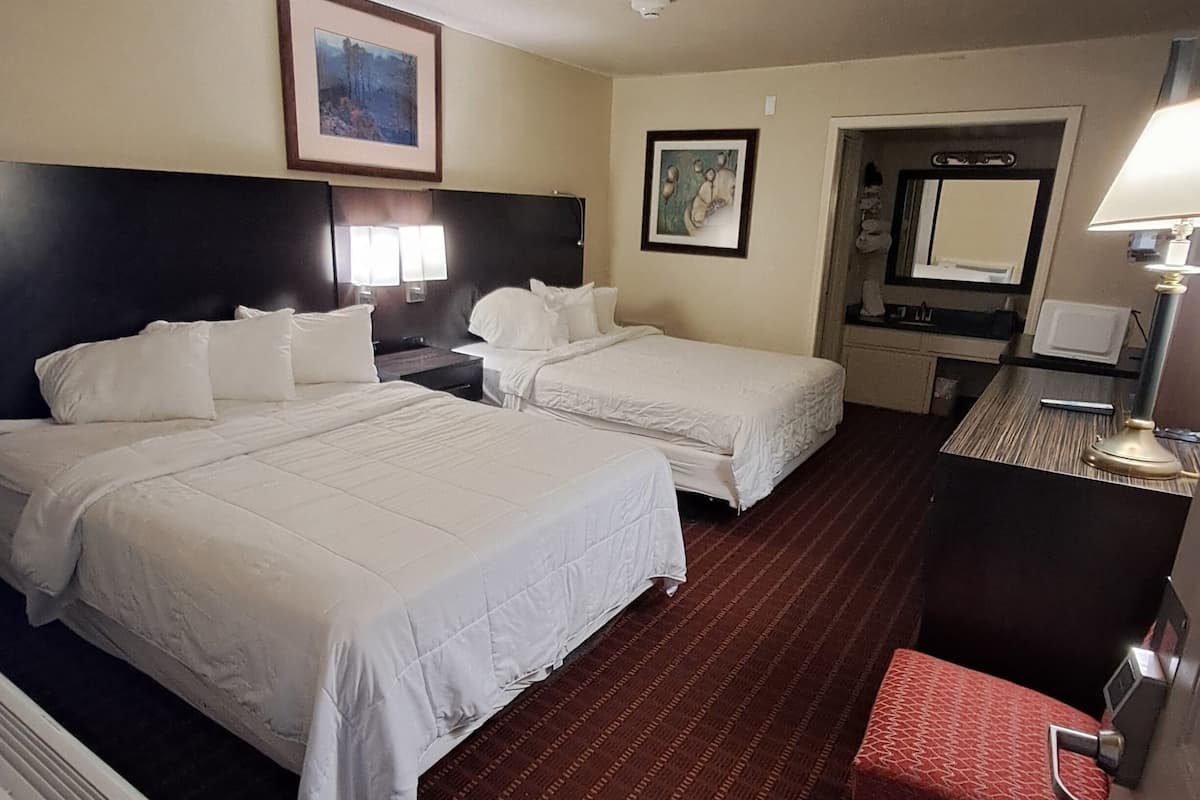 A hotel room with two beds, a desk, a chair, a mirror, and a picture on the wall.