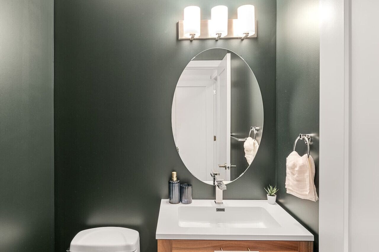 Een moderne badkamer met een donkere muur, een witte wastafel, een grote spiegel en een handdoekrek.